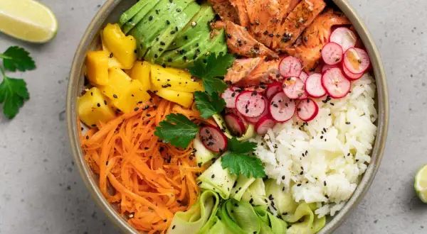 Un bol coloré avec saumon, avocat, mangue, carottes râpées, radis, courgette et riz blanc. Parfait pour des menus semaine famille équilibrés et savoureux.