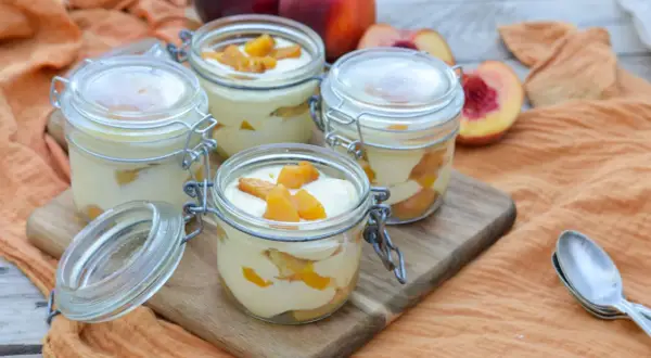Quatre verrines de tiramisu pêche, garnies de morceaux de fruits frais. Un délice estival.