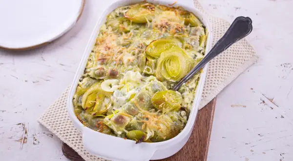 Plat gratiné de ravioles aux poireaux, une recette de Laurent Mariotte, servi dans un plat blanc avec une cuillère.