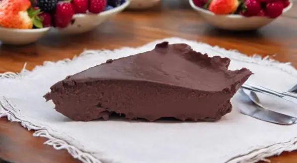 Tranche de gâteau au chocolat onctueux, servi avec des fruits rouges frais en arrière-plan. Un délice inattendu, ce gâteau courgette surprend par sa texture.