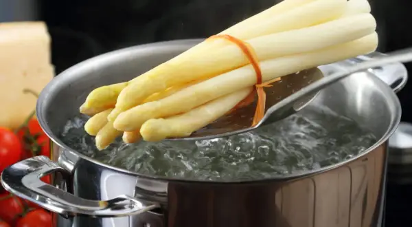 Un bouquet d'asperges blanches est plongé dans l'eau bouillante pour une cuisson parfaite.