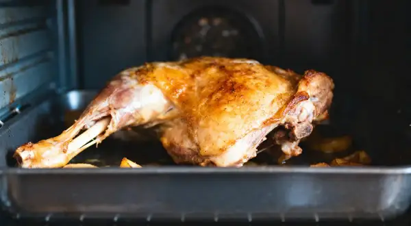 Gigot d'agneau doré, prêt pour la cuisson au four. La peau croustillante promet un délice.