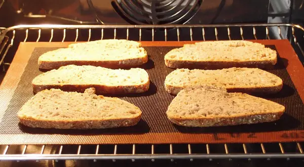 Six tranches de pain de campagne, prêtes pour la décongélation pain four, sur une plaque en silicone dans un four chaud.