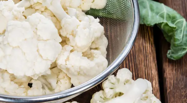 Chou-fleur frais coupé en bouquets dans une passoire, prêt pour la cuisson. Eau froide ou chaude, le choix dépend de la recette.