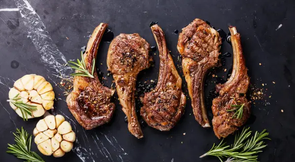 Quatre côtelettes d'agneau grillées, assaisonnées et garnies de romarin, avec des têtes d'ail rôties. La cuisson côtelette agneau parfaite.