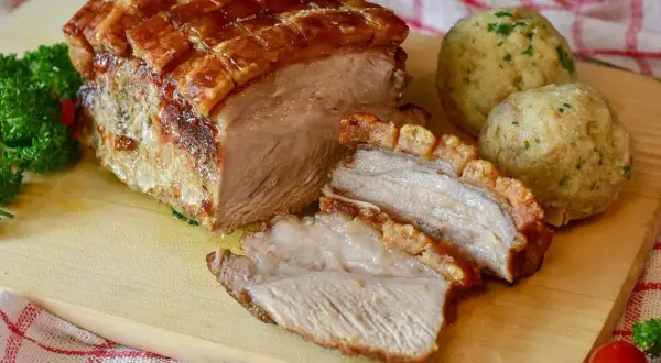 Rôti de porc croustillant, coupé en tranches, servi avec des boules de pain et du persil. Le temps de cuisson du rôti de porc est parfait.
