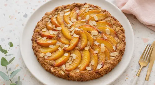Tarte tatin aux pêches, garnie d'amandes effilées. Un délice doré et fruité.