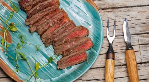 Tranches d'onglet de bœuf saignant, parsemées de gros sel, sur une assiette turquoise. Une fourchette et un couteau à steak sont à droite.