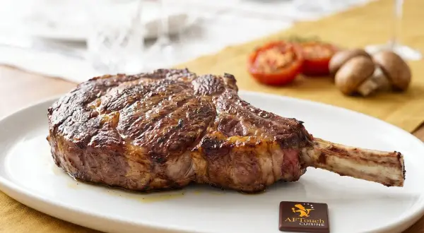 Un magnifique côte de bœuf, prêt à être dégusté. Grillé à la perfection, il attend patiemment sur une assiette blanche, accompagné de tomates et de champignons.