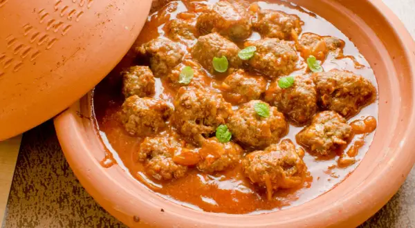 Un plat de tajine kefta, des boulettes de viande mijotées dans une sauce tomate épicée, garni de feuilles de menthe fraîche.