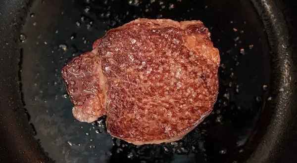 Un beau morceau de Black Angus en cuisson dans une poêle, avec des cristaux de sel qui fondent.