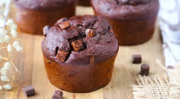 Gros plan sur un muffin banane chocolat moelleux, parsemé de pépites de chocolat, sur une planche en bois.