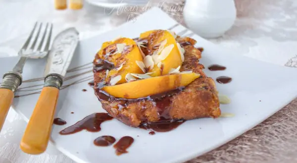 Une délicieuse brioche perdue, nappée de chocolat et garnie de fruits et d'amandes effilées, prête à être dégustée.