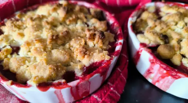 Deux petits ramequins de crumble aux quetsches, aux bords rouges et blancs, sur un torchon à rayures rouges.