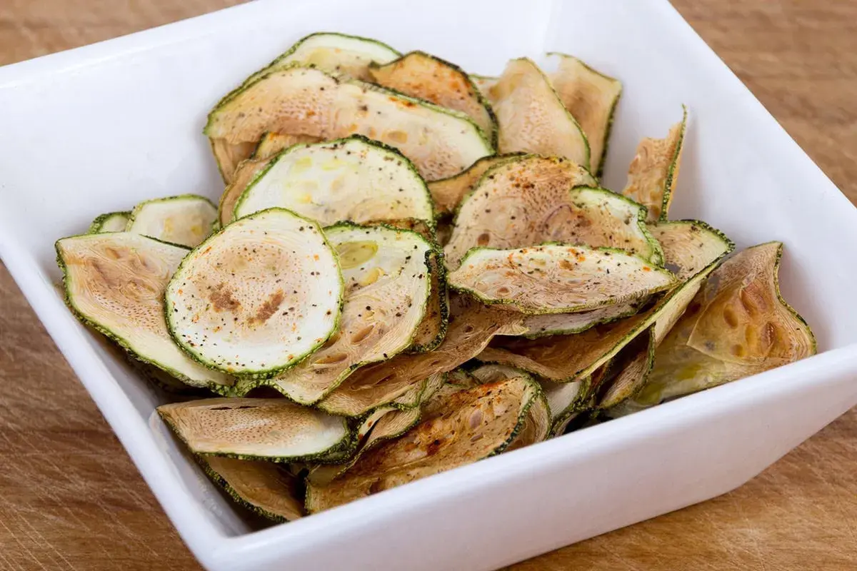 Un bol blanc rempli de chips de courgette croustillantes, assaisonnées d'épices.
