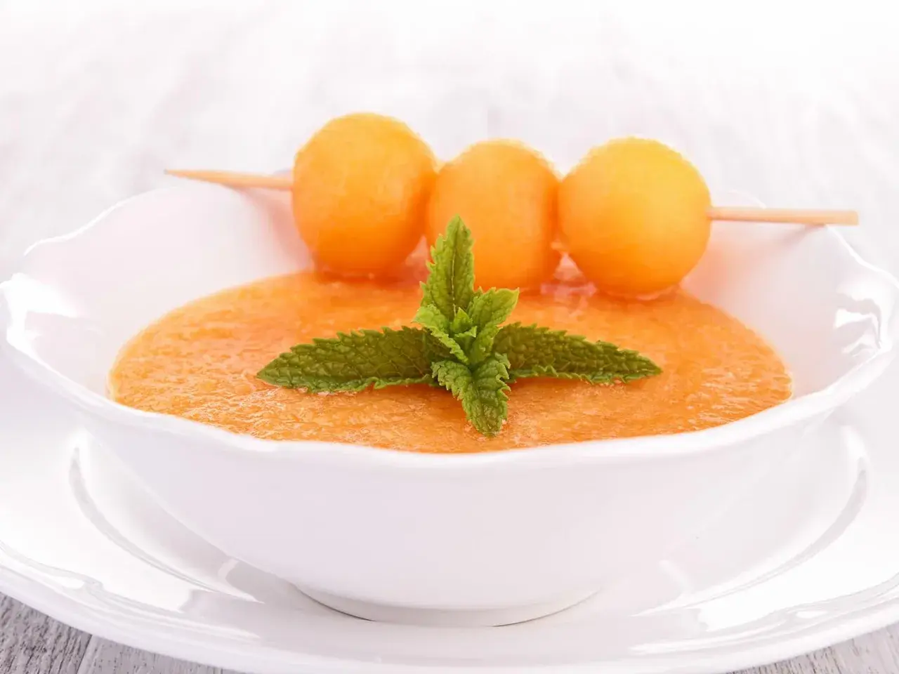 Un bol de gaspacho de melon, garni de feuilles de menthe et de billes de melon sur une brochette. Rafraîchissant et coloré.