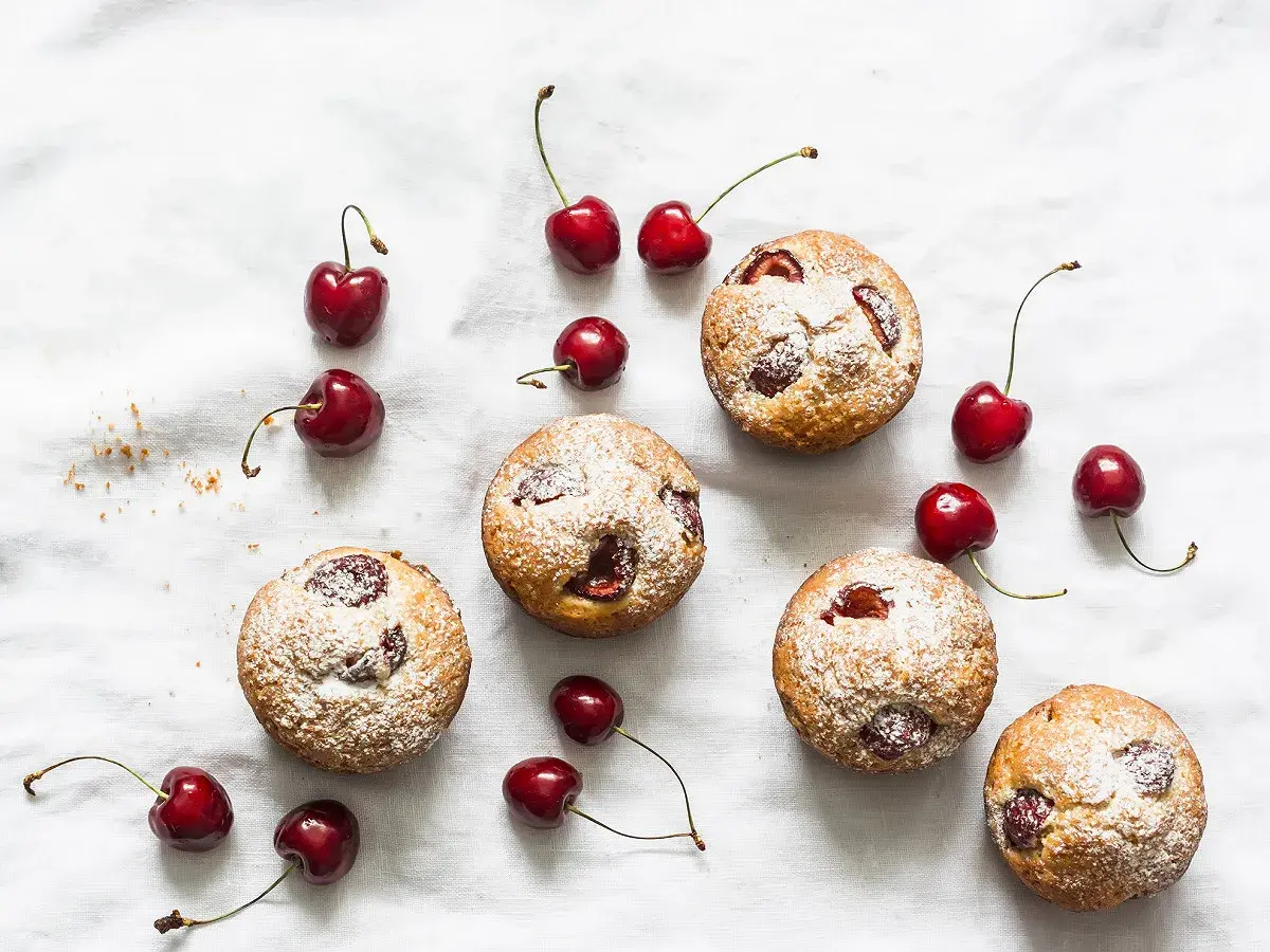 Financiers aux cerises saupoudrés de sucre glace, disposés avec des cerises fraîches sur un tissu blanc.