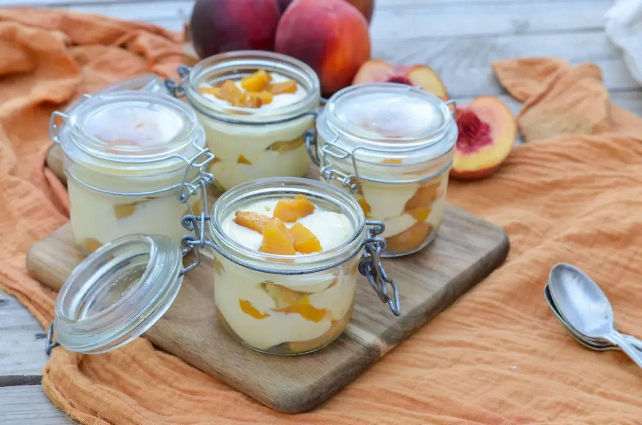Quatre verrines de tiramisu pêche, garnies de morceaux de fruits frais. Un délice estival.