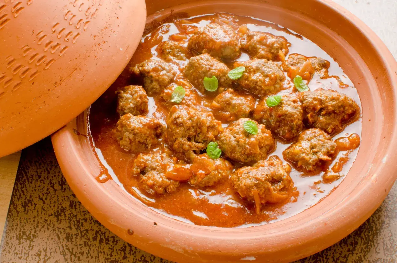 Un plat de tajine kefta, des boulettes de viande mijotées dans une sauce tomate épicée, garni de feuilles de menthe fraîche.