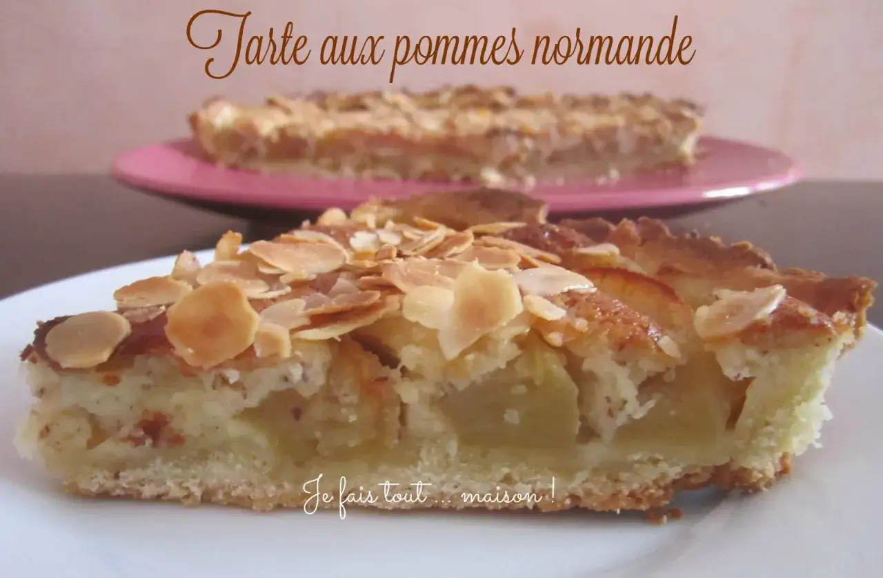 Une part de tarte normande aux pommes, garnie d'amandes effil&eacute;es, sur une assiette blanche. Une autre tarte est visible en arri&egrave;re-plan.