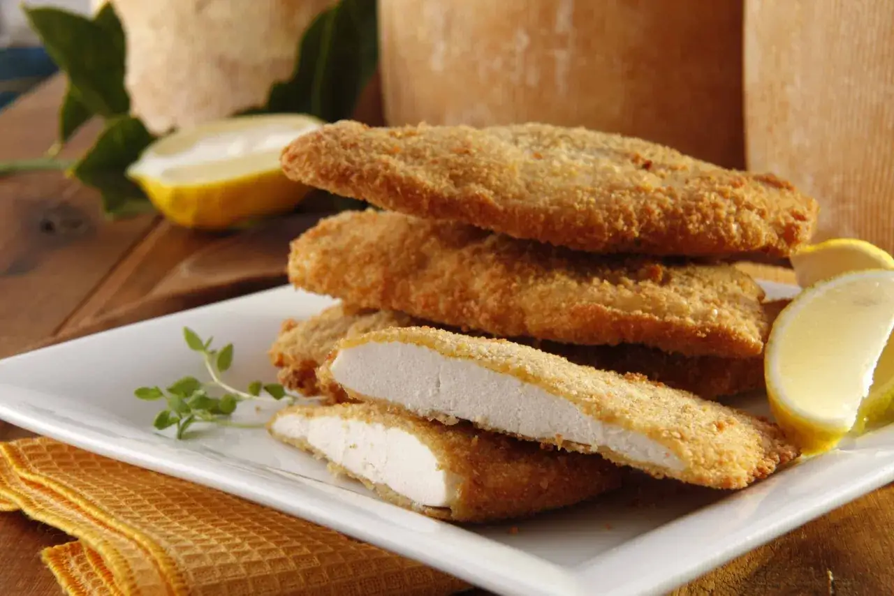 Escalopes pan&eacute;es dor&eacute;es, pr&ecirc;tes pour une recette escalope milanaise. Servies avec des quartiers de citron et une touche de verdure.