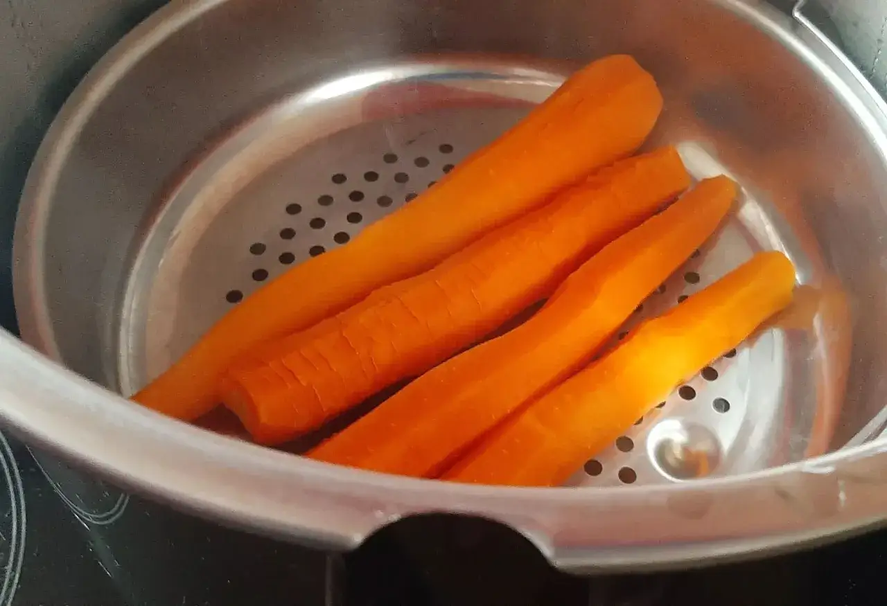 Carottes pelées prêtes pour la cuisson à la cocotte minute. Elles sont disposées dans un panier vapeur en métal.