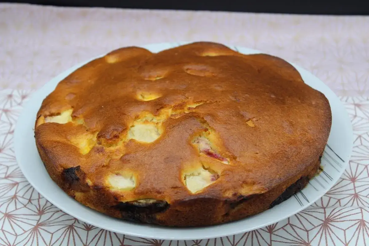 Gâteau rond doré aux morceaux de fruits visibles, posé sur une assiette blanche.