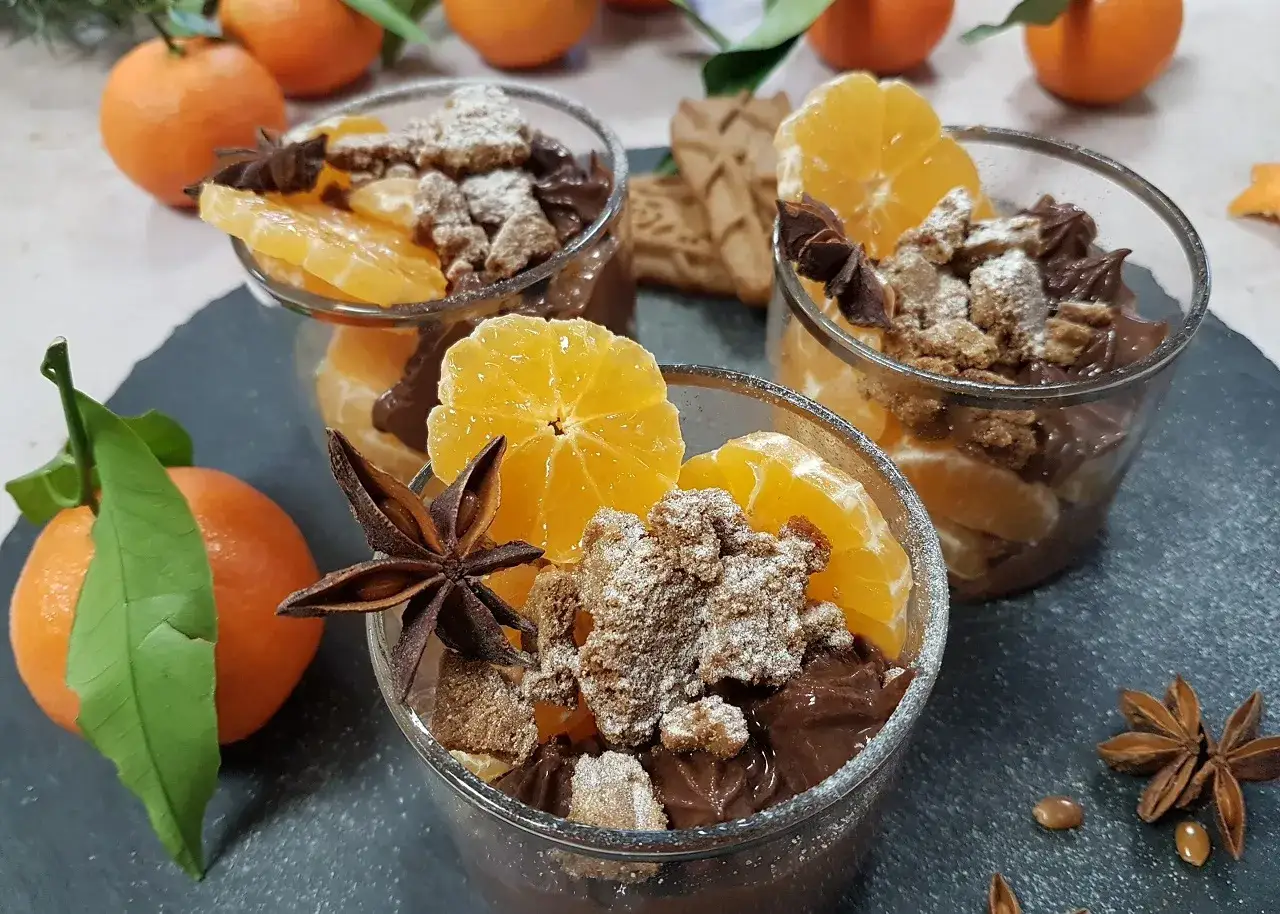 Trois verrines de mousse au chocolat garnies de quartiers d'orange, de miettes de biscuits et d'anis étoilé.