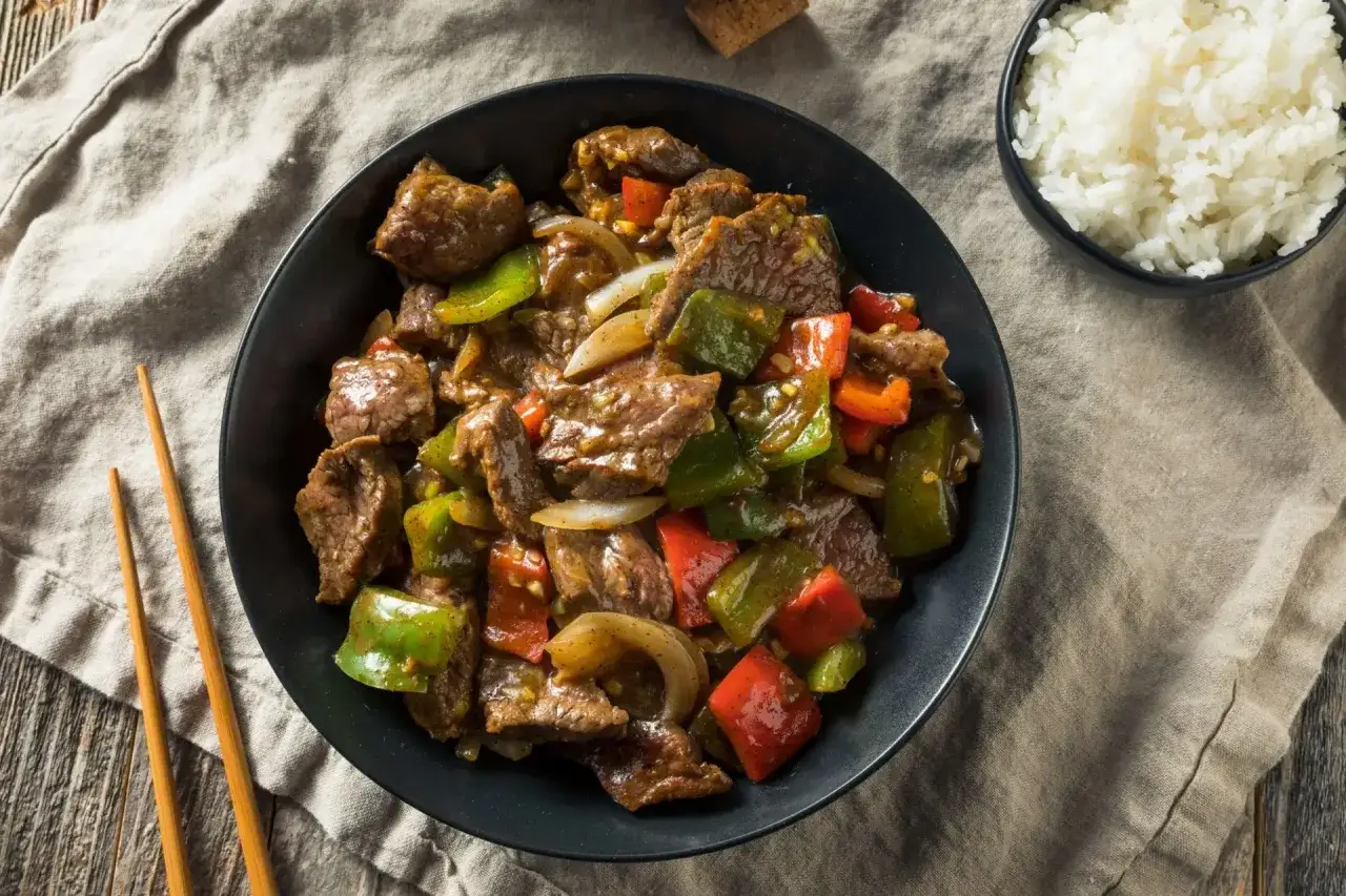 Un d&eacute;licieux saut&eacute; de b&oelig;uf aux poivrons verts et rouges, servi avec du riz blanc et des baguettes.
