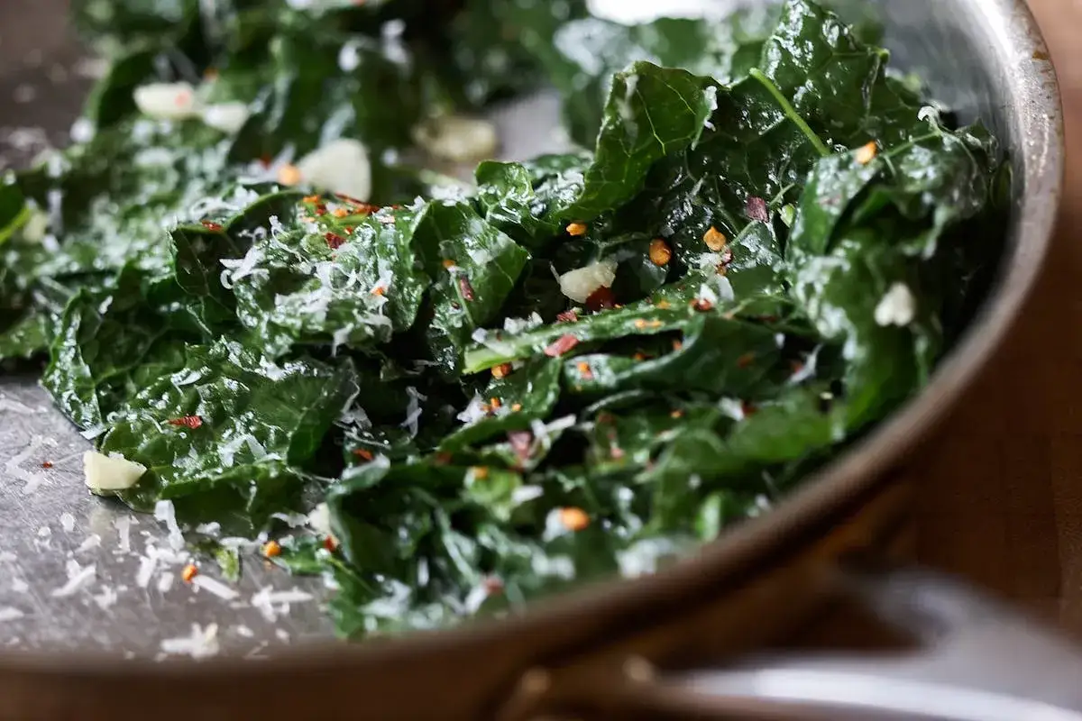 Chou vert frisé, assaisonné d'ail et de flocons de piment rouge, est en cours de cuisson dans une poêle.