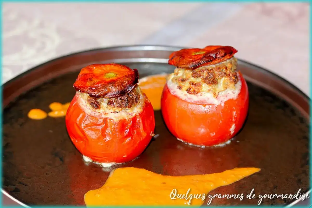 Deux tomates farcies, une recette de Laurent Mariotte, garnies d'une farce savoureuse et gratinée, servies sur une assiette avec une sauce orangée.