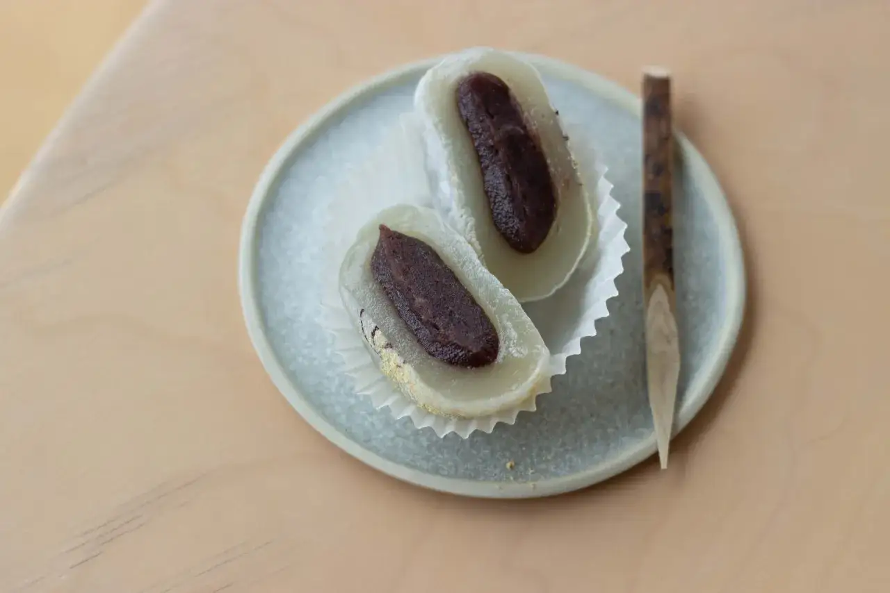 Deux mochis &agrave; la p&acirc;te de haricots rouges, servis sur une assiette avec un petit b&acirc;ton en bois. Une d&eacute;licieuse mochi recette.