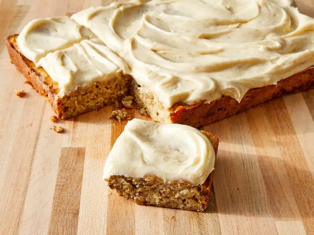 Un délicieux gâteau à la banane, généreusement glacé, est coupé sur une planche en bois. Une part est déjà servie.