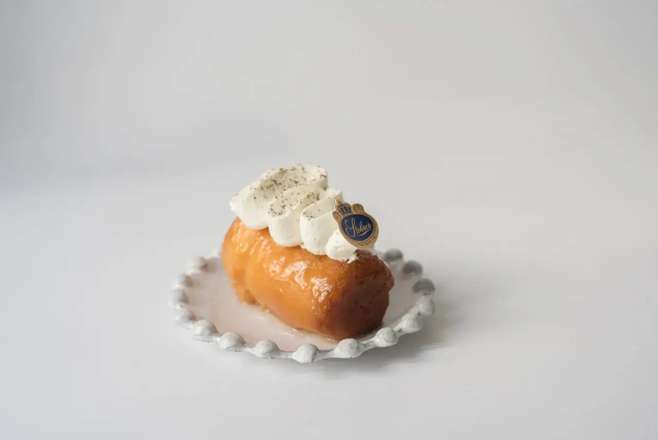 Un baba au rhum, un classique de la p&acirc;tisserie fran&ccedil;aise, garni de cr&egrave;me fouett&eacute;e et d'une touche de cannelle, sur une assiette d&eacute;corative.