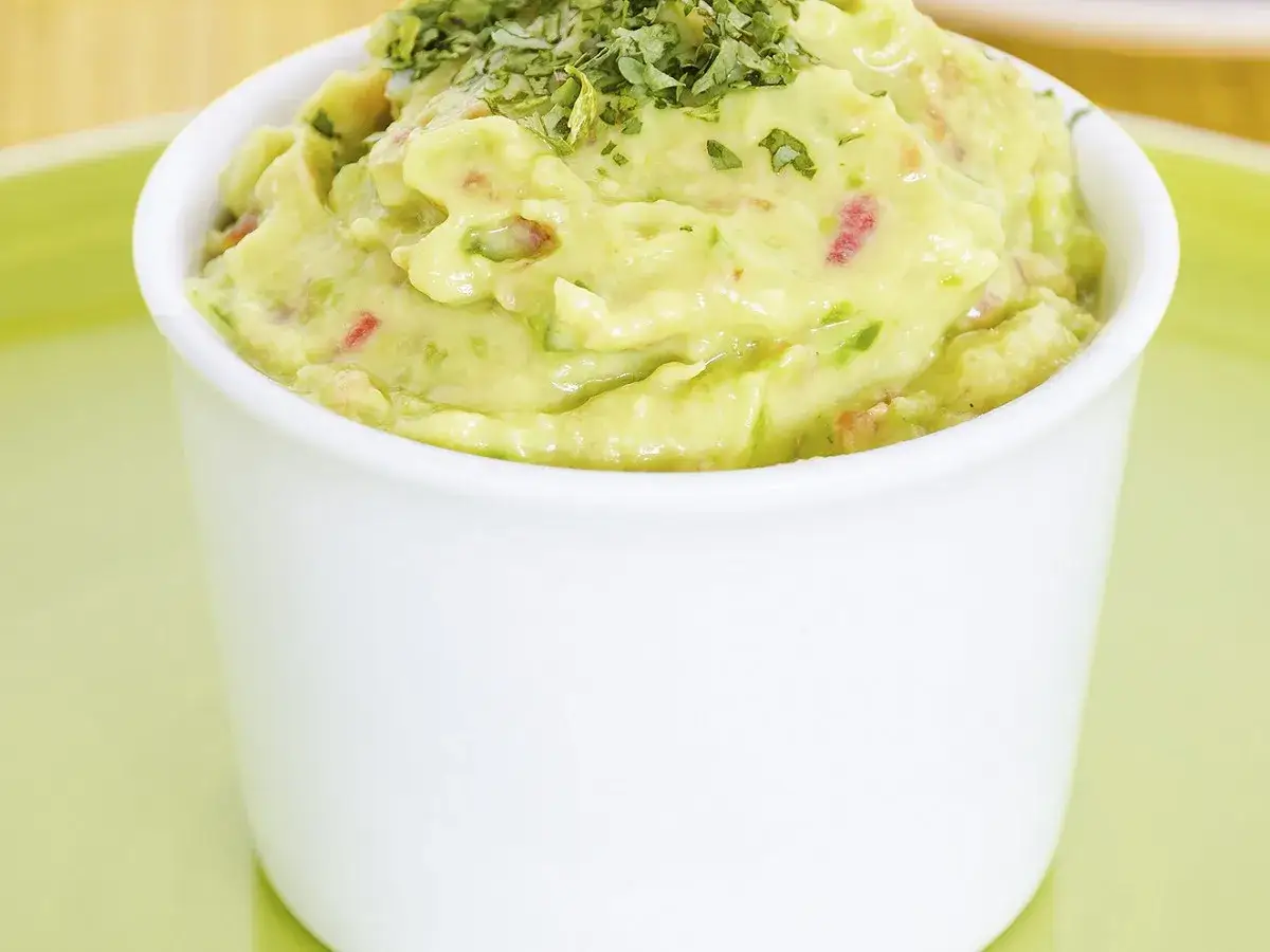 Un bol de guacamole traditionnel, garni de coriandre fraîche. Parfait pour accompagner vos chips !
