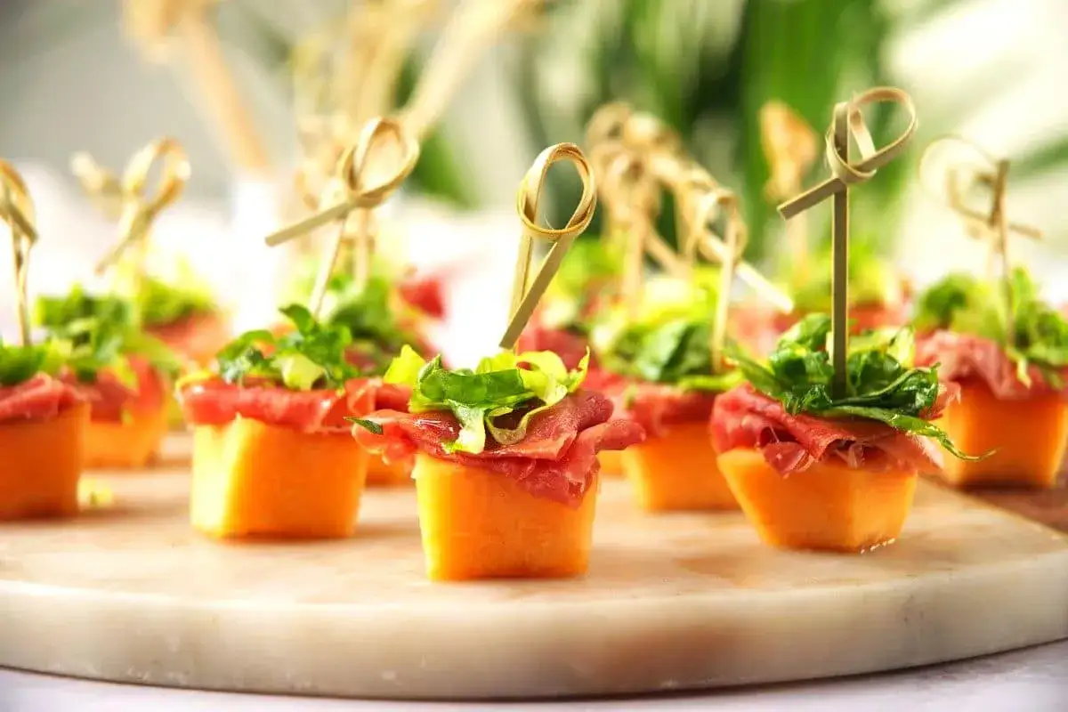 Petits cubes de melon recouverts de fines tranches de prosciutto et de verdure, parfaits pour une recette melon facile et &eacute;l&eacute;gante.