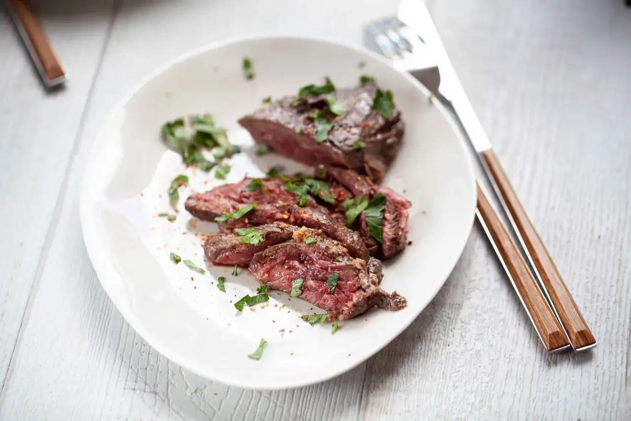 Un onglet de bœuf tranché, garni de persil frais et d'épices, prêt à être dégusté. Une recette parfaite pour une marinade pour onglet de boeuf.
