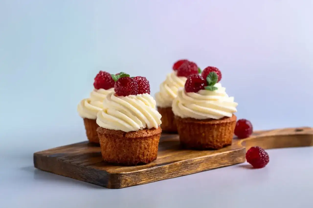 Quatre cupcakes gourmands avec gla&ccedil;age blanc et framboises, parfaits pour une recette facile.