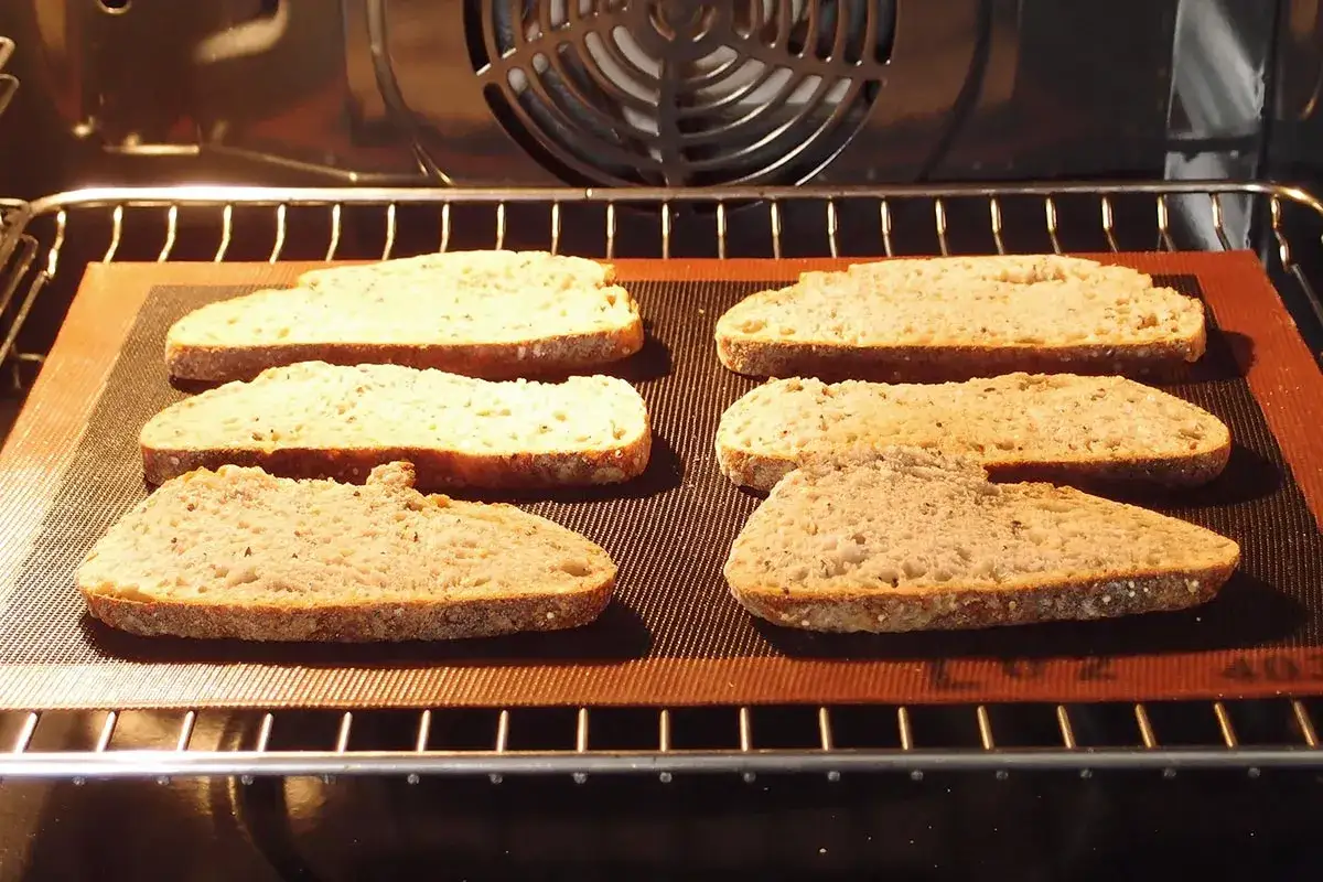 Six tranches de pain de campagne, pr&ecirc;tes pour la d&eacute;cong&eacute;lation pain four, sur une plaque de cuisson dans un four.