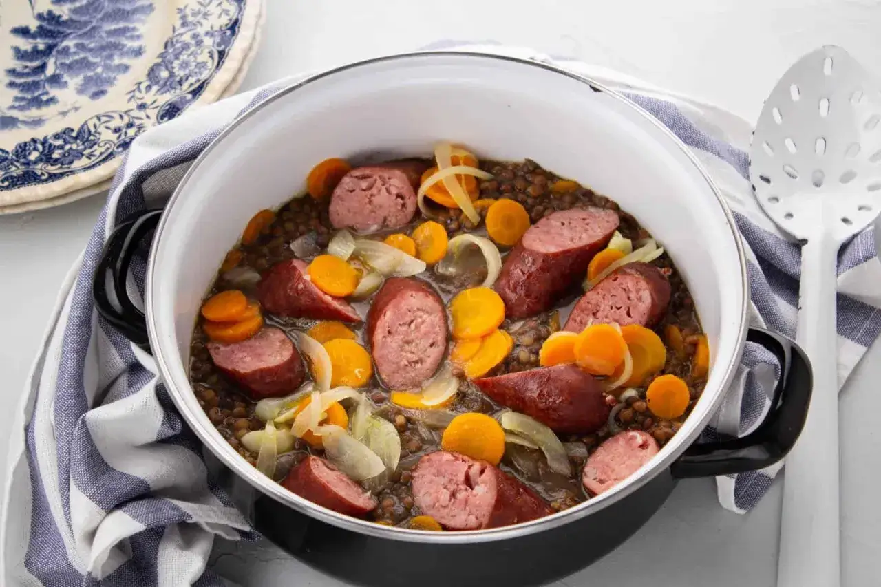 Un plat de lentilles saucisses mijoté dans une cocotte, avec des rondelles de carottes et des oignons. Un délice réconfortant.