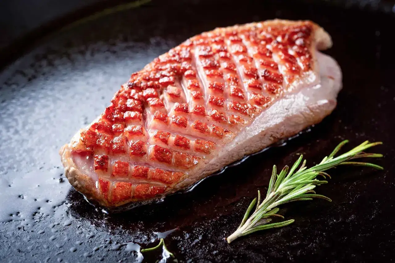 Magret de canard doré et croustillant dans une poêle, avec une branche de romarin. Idéal pour le temps de cuisson magret de canard parfait.
