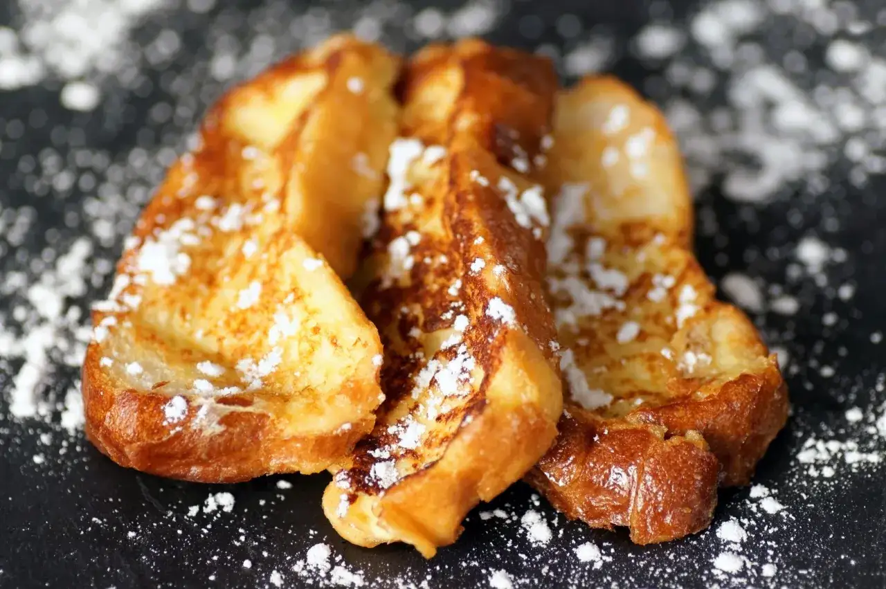 Trois tranches dorées de brioche perdue saupoudrées de sucre glace, un délice simple et réconfortant.