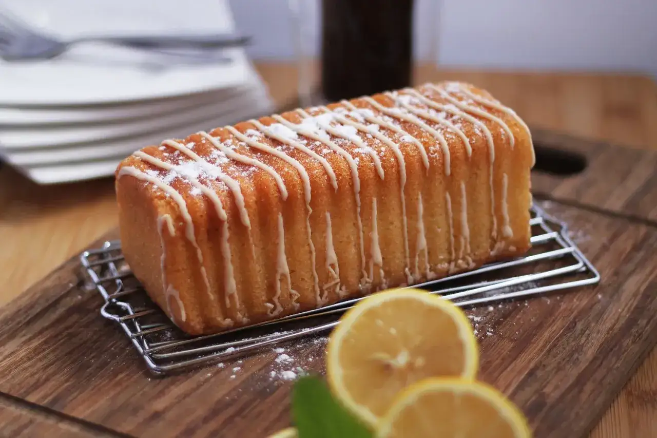Un g&acirc;teau moelleux au citron grand-m&egrave;re, glac&eacute; et saupoudr&eacute; de sucre glace, sur une grille, avec des citrons frais en avant-plan.