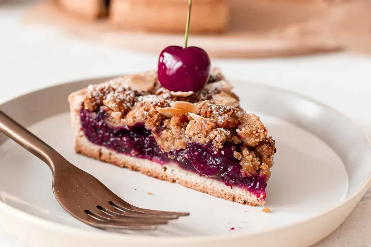 Tranche de tarte aux cerises &agrave; l'ancienne, garnie d'une cerise fra&icirc;che et saupoudr&eacute;e de sucre glace et d'amandes effil&eacute;es.