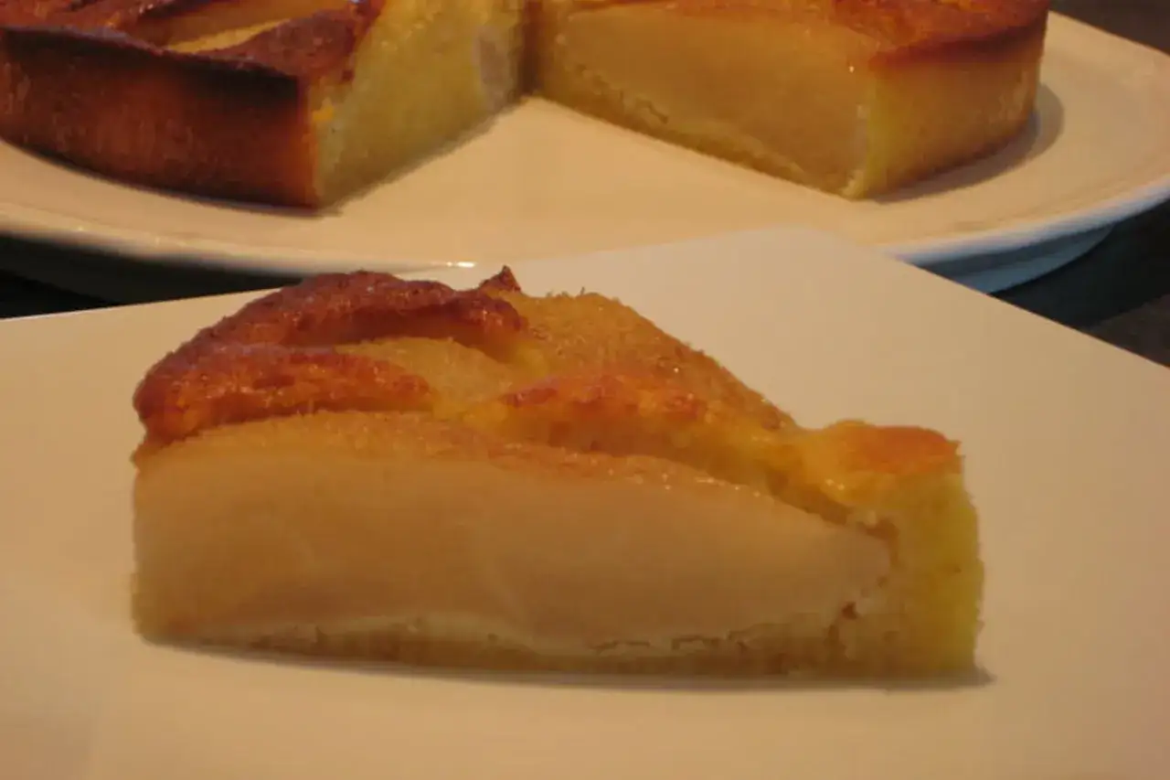 Une part de gâteau aux poires, avec des poires tendres et une croûte dorée, sur une assiette blanche.