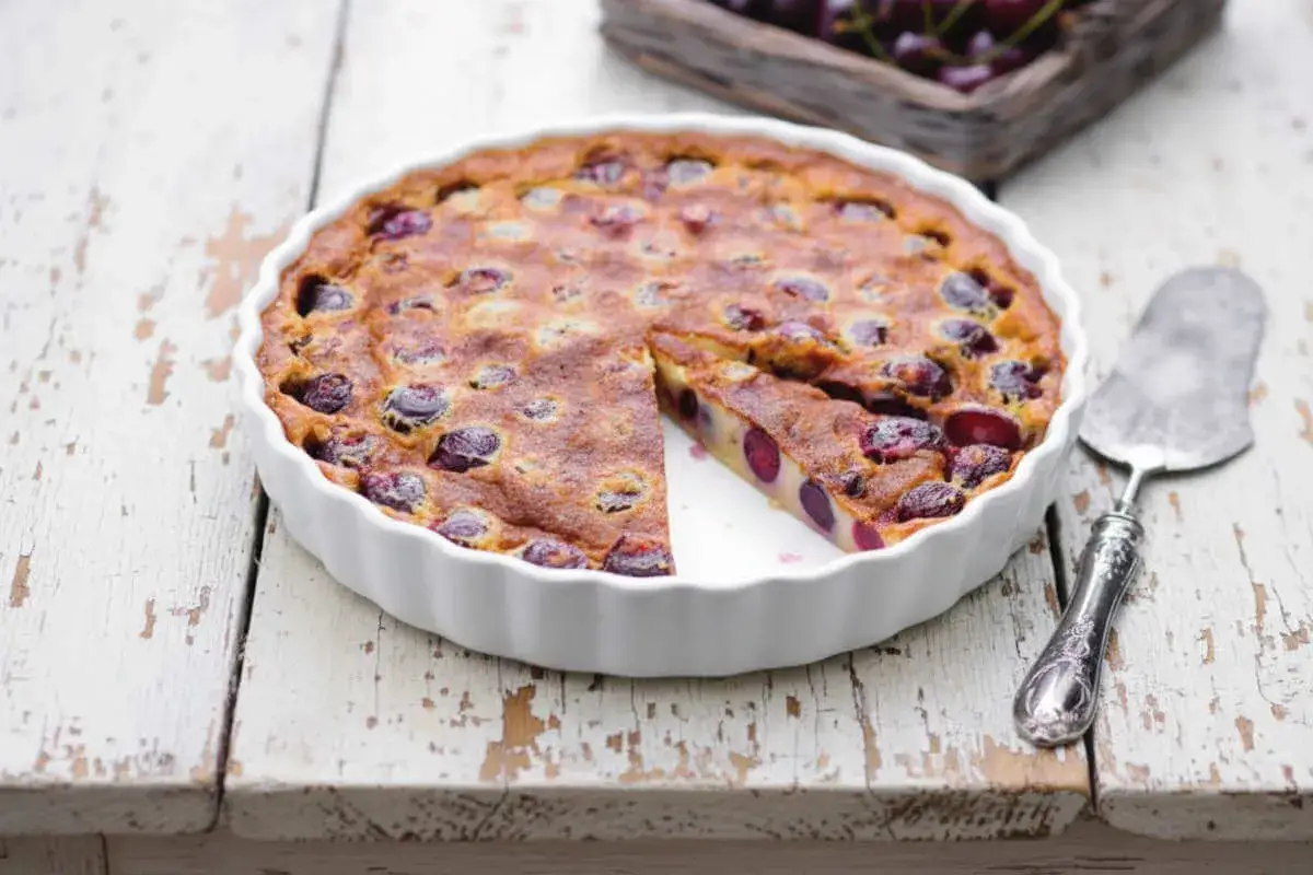 Un clafoutis aux cerises moelleux et léger, tout juste sorti du four, avec une part coupée pour révéler ses fruits juteux.