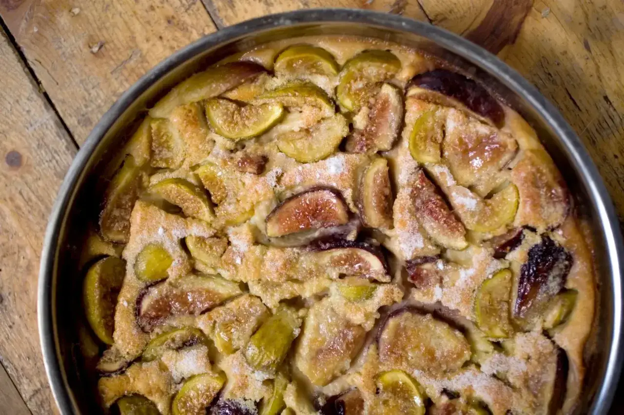 Un délicieux clafoutis aux figues, tout juste sorti du four, parsemé de sucre glace sur sa croûte dorée.