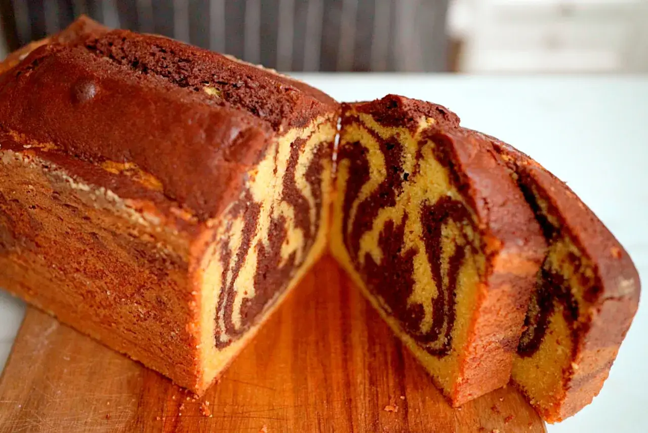 Un délicieux gâteau marbré, coupé en deux, révèle ses motifs tourbillonnants de chocolat et de vanille sur une planche en bois.