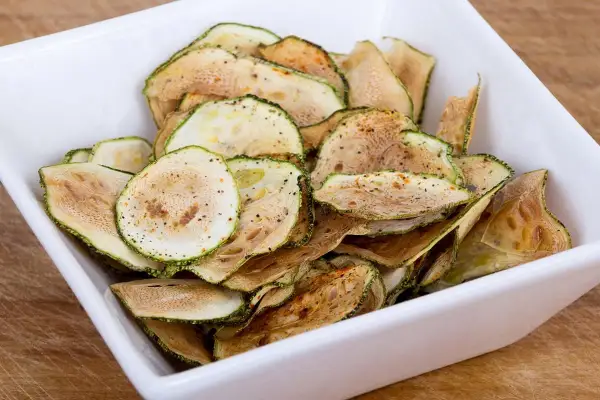 Un bol blanc rempli de chips de courgette croustillantes, assaisonnées d'épices.