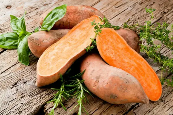 Patates douces coupées, prêtes pour la cuisson à l'eau bouillante, garnies de basilic et de thym frais sur fond de bois rustique.
